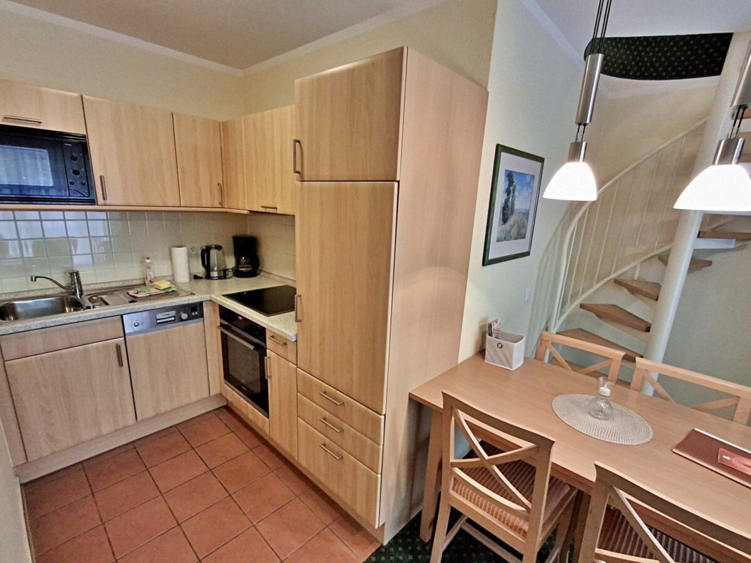 Une cuisine compacte avec des meubles en bois, un four encastré, un évier et un coin repas comprenant une table et des chaises.