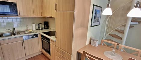 Cocina compacta con muebles de madera, horno empotrado, pileta y comedor con mesa y sillas.