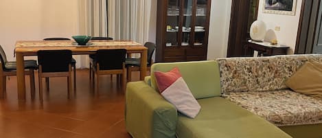 A living room with a green sofa, a dining table with chairs, and a cabinet.