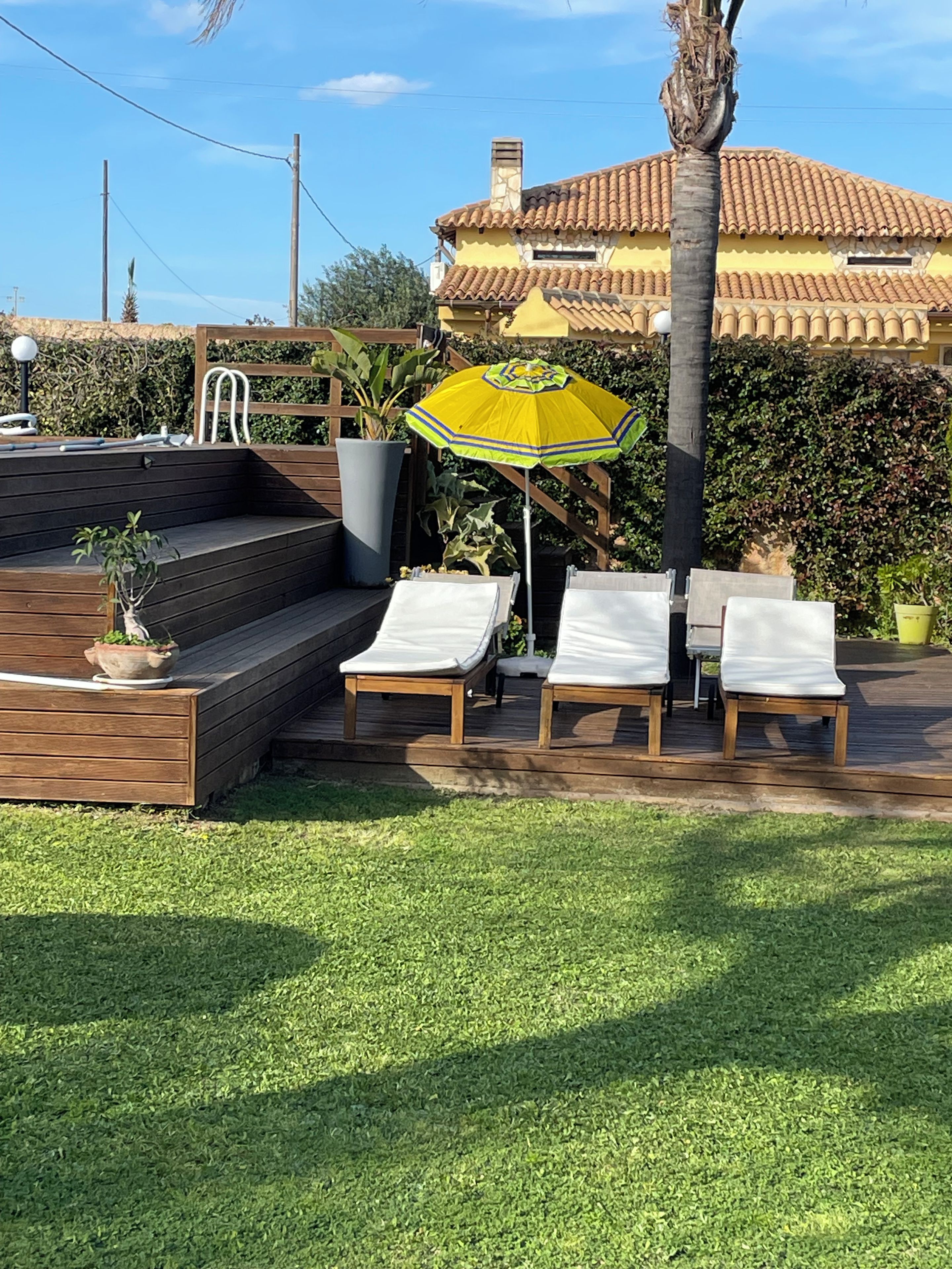 Een houten terras met buitenmeubels en een gele parasol.