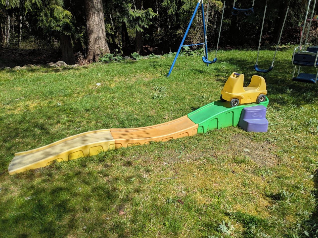 Lasten liukumäki vehreällä ulkoalueella, taustalla puita.