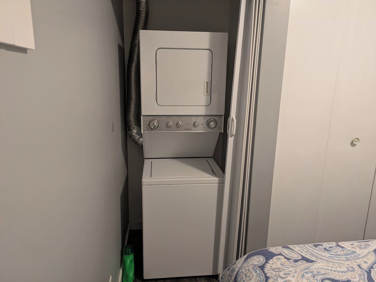 A compact laundry area with a washer and dryer, a patterned bed, and a door leading to another room.