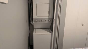 A compact laundry area with a washer and dryer, a patterned bed, and a door leading to another room.