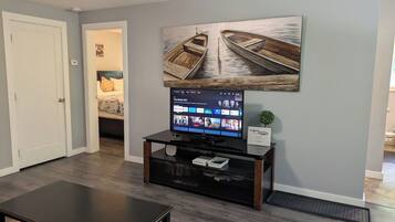 A living room with a flat-screen TV on a black stand, a coffee table, and a wall-mounted painting of boats.