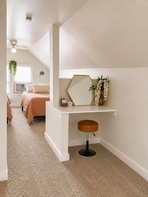 A bedroom with a bed, a desk, a chair, a hanging plant, and a ceiling fan.