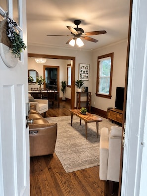 A living room with a ceiling fan, a dining area, and a kitchen visible through an open door.