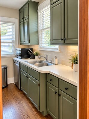 A kitchen with green cabinets, a stainless steel sink, and a microwave.