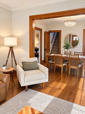 A living room with a sofa, a dining table with chairs, a lamp, and a staircase leading to another room.