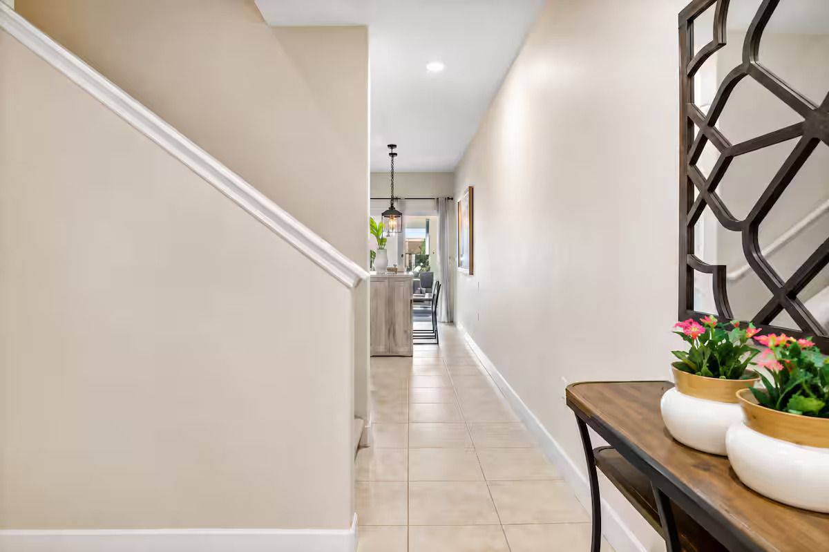 A hallway with a staircase, a dining table with potted plants, and a decorative wall panel.