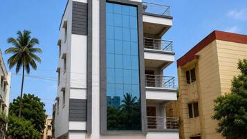 A multi-story building with a central glass facade, balconies on the upper floors, and a gated entrance.
