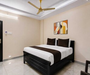 A modern bedroom with a black bed, white bedding, a ceiling fan, and two abstract paintings on the wall. - Suite Room Balaji Guest House (Visakhapatnam)