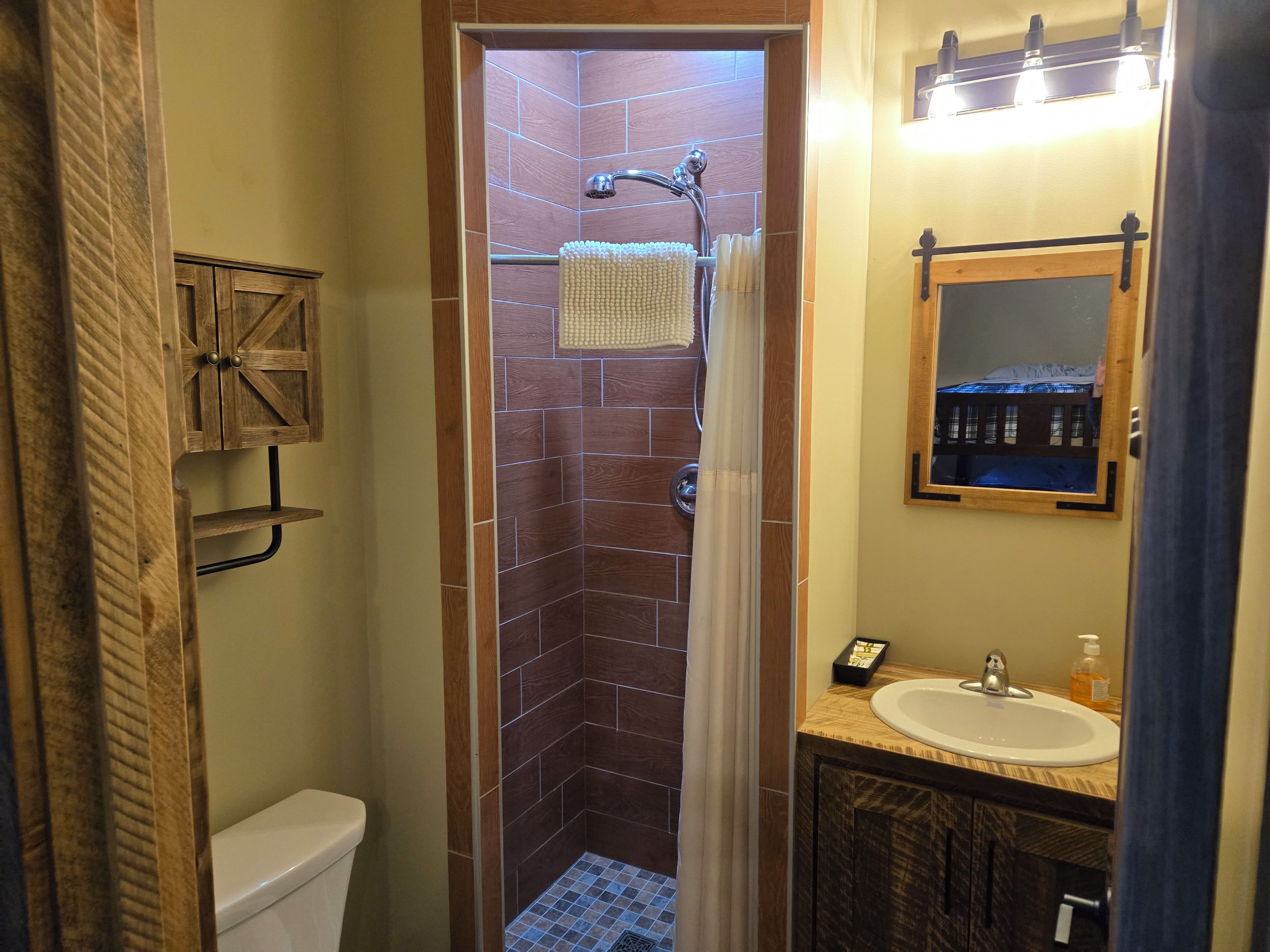 A bathroom with a shower, toilet, sink, and a mirror.