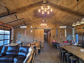 Un intérieur chaleureux avec un plafond en bois, un canapé en cuir, un coin bar en bois et une cuisine en arrière-plan.