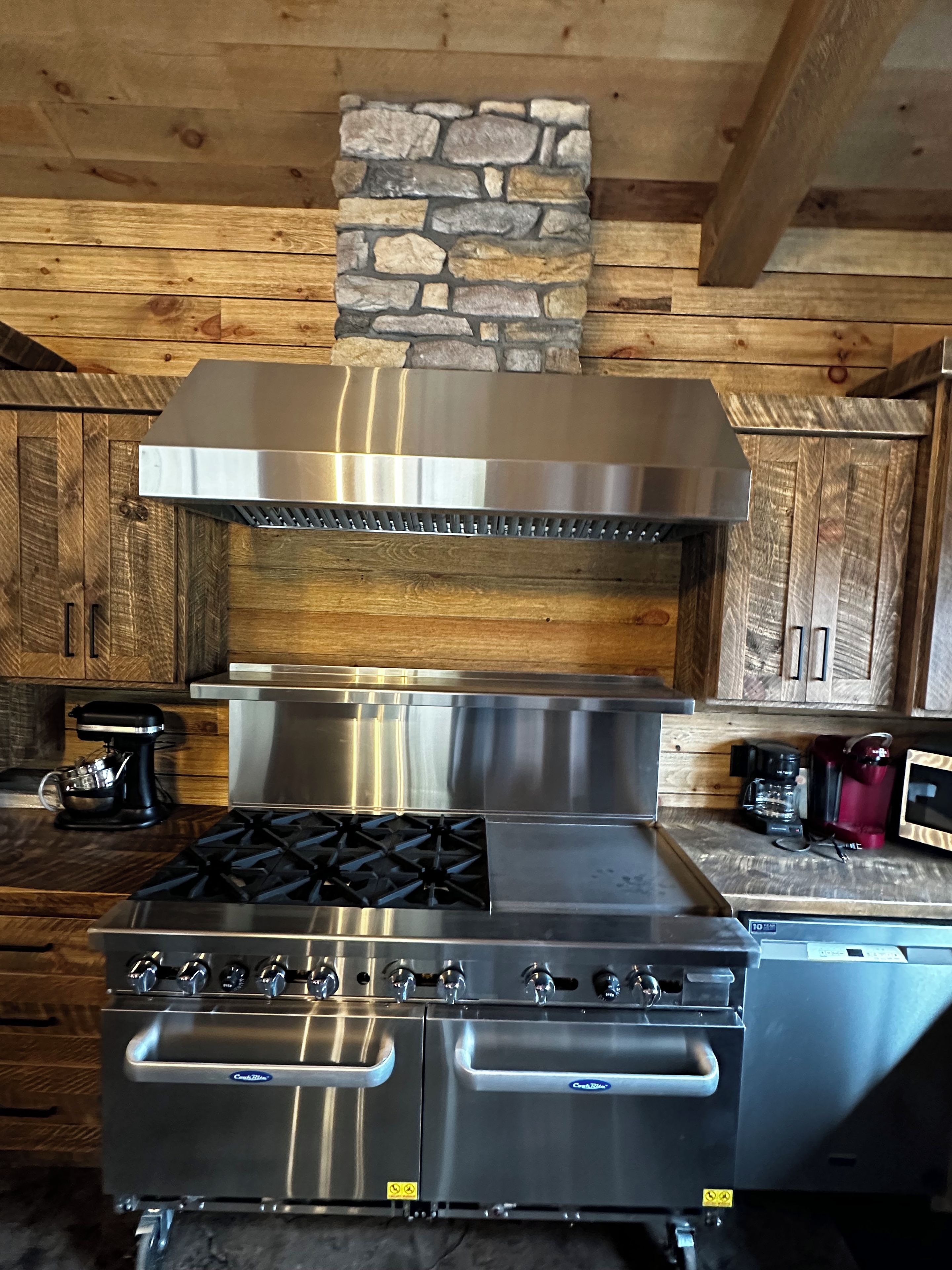 A kitchen with a stainless steel range, a stone accent wall, wooden cabinets, and a coffee maker.