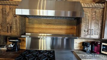 A kitchen with a stainless steel range, a stone accent wall, wooden cabinets, and a coffee maker.