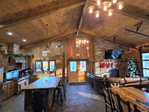 A rustic interior with a wooden ceiling, stone fireplace, and a bar area with stools.