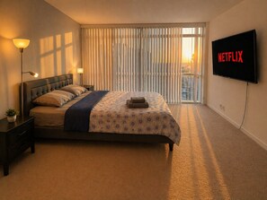 A hotel room with a bed, bedside lamps, a TV, and a view of the city through large windows. - Spacious 2BR Downtown Toronto Apartment | Parking (Toronto)