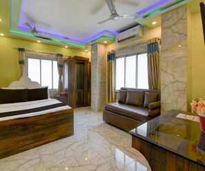 Ein Hotelzimmer mit einem Bett, einem Sofa, einem Schreibtisch, einem Deckenventilator und einem Fenster mit Vorhängen.