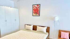 Een slaapkamer met een bed, een kledingkast, een nachtkastje, een lamp en een foto aan de muur.
