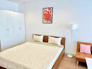 A bedroom with a bed, a wardrobe, a bedside table, a lamp, and a picture on the wall. - AIGO LUXURY APARTMENT (ho chi minh)