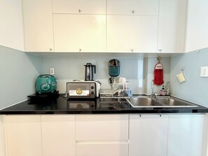 A kitchen with white cabinets, a black countertop, a toaster, a kettle, and a sink. - AIGO LUXURY APARTMENT (ho chi minh)