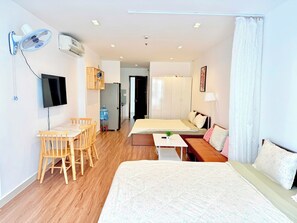 A hotel room with a bed, a sofa, a dining table with chairs, a TV, a water dispenser, and a ceiling fan. - AIGO LUXURY APARTMENT (ho chi minh)