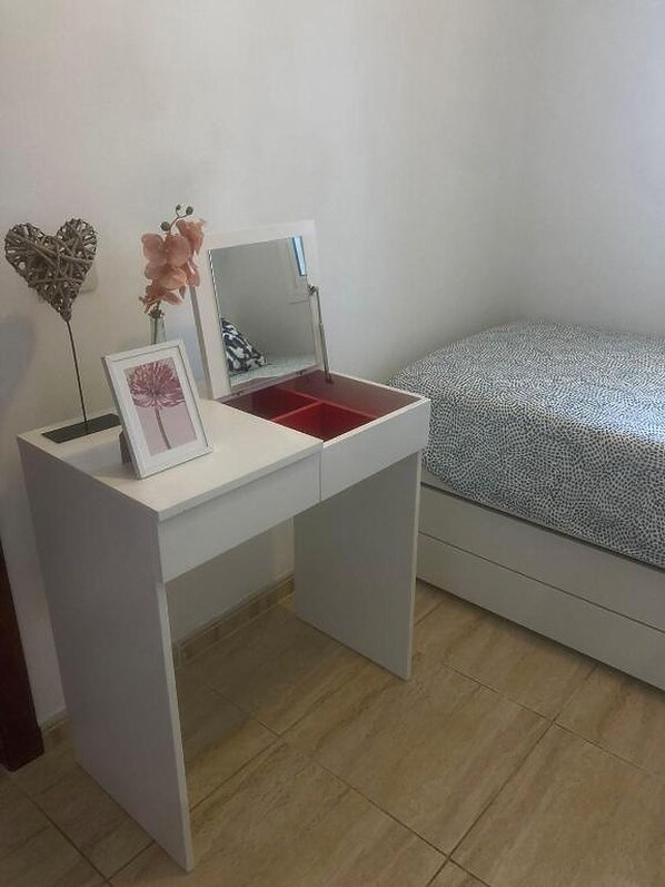 A white desk with a mirror, a framed picture, and a pink flower.
