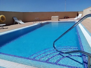 Une piscine à l’eau d’un bleu cristallin, avec une échelle en métal et des chaises longues blanches.