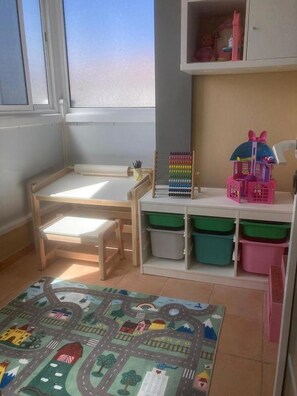 Ein Kinderzimmer mit einem Holztisch, Regalen, Aufbewahrungsboxen und einer Spielmatte.