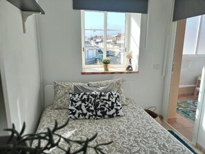 A bedroom with a bed, a window with a view of the street, and a potted plant on the windowsill. - Chalet Ocean – Ocean view, pool, direct access to the ocean (CN)