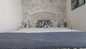 A bedroom with a bed, two bedside tables, a headboard, and a wall-mounted artwork.