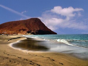 A beach with a large hill in the background and footprints leading into the water. - Chalet Ocean – Ocean view, pool, direct access to the ocean (CN)