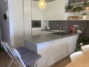 Une cuisine moderne dotée d’un îlot central, d’appareils électroménagers en acier inoxydable et d’un luminaire suspendu.