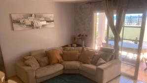 A living room with a beige sectional sofa, a dark blue rug, and a painting on the wall.