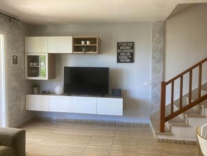 Ein Wohnzimmer mit einem Flachbildfernseher auf einer weißen Unterhaltungsanlage, einer Treppe rechts und einem Schild an der Wand.