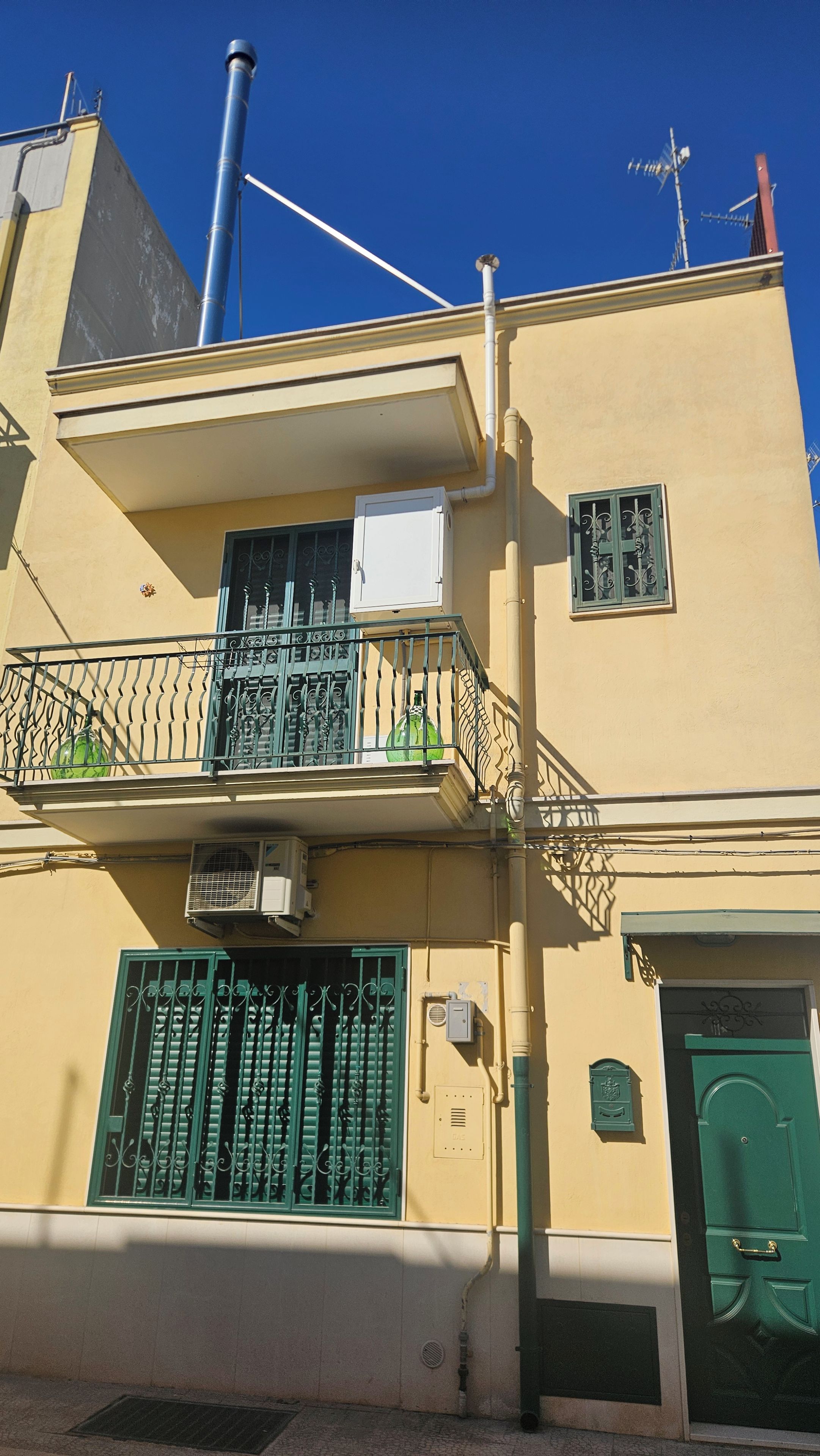 Un immeuble de deux étages doté d’un balcon, d’une porte verte et d’une petite fenêtre ornée d’une grille métallique.