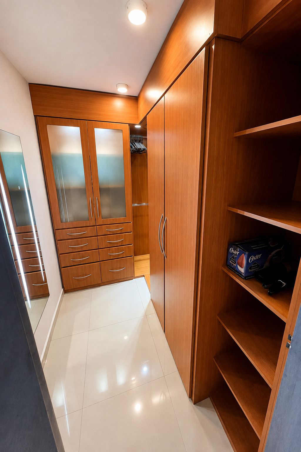 A walk-in closet with wooden cabinets, a mirrored closet door, and a shelf with a box.