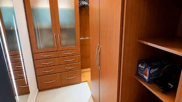 A walk-in closet with wooden cabinets, a mirrored closet door, and a shelf with a box.