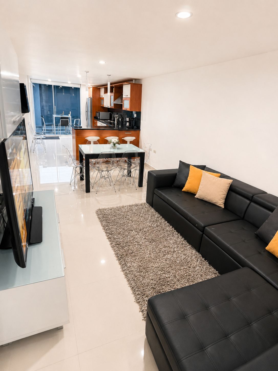 A modern living room with a black sofa, a glass coffee table, and a grey rug.