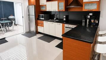 A modern kitchen with a central island, wooden cabinets, and a stainless steel refrigerator.