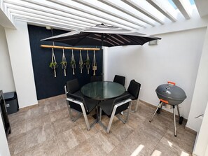 Ein moderner Essbereich im Freien mit einem runden Tisch, Stühlen, einem Grill und hängenden Pflanzen aus Makramee.