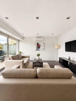 Ein modernes Wohnzimmer mit einer Sofagarnitur, einem Couchtisch, einer Stehlampe und einem flachbildfernseher an der Wand.