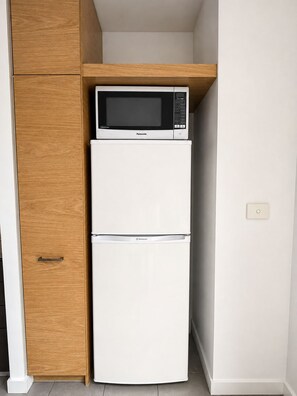 Eine kleine Küche mit einem weißen Kühlschrank und einer Mikrowelle darüber.