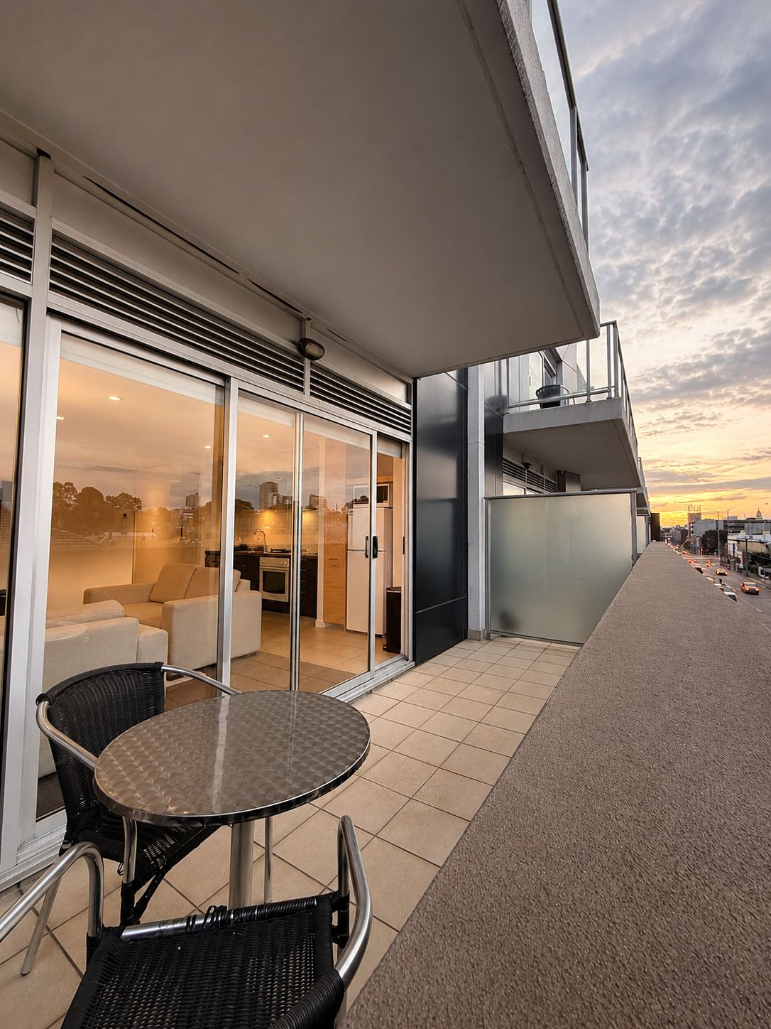 Ein moderner Balkon mit Zugang zur Küche durch eine Glastür, einem runden Tisch mit Stühlen und Blick auf die Stadt.