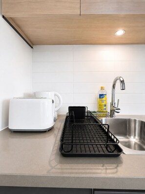 Eine Küche mit einem Toaster, einem Wasserkocher, einem Geschirrgestell, einer Flasche Spülmittel und einem Edelstahl-Spülbecken.
