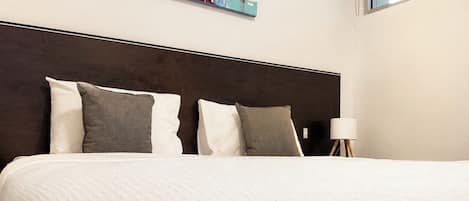 A hotel room with a large bed, a modern headboard, a colorful abstract painting on the wall, and a window providing natural light.