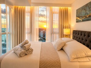 Hotellihuone, jossa on suuri sänky, näköala kaupungin ylle ja taulu seinällä.