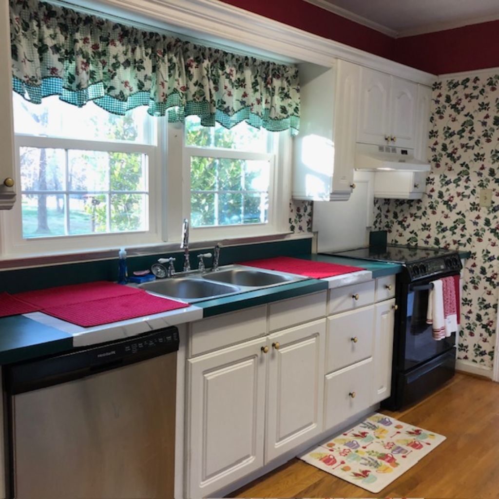 A kitchen with white cabinets, a black stove, and a window with a floral curtain.