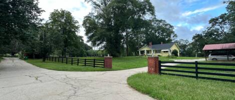 A paved driveway leading to a house with a fenced yard and a covered structure.