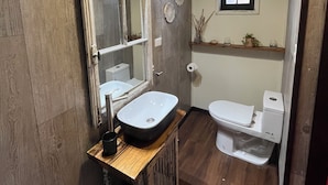Une salle de bain avec un meuble-lavabo en bois, un lavabo blanc, un miroir, des toilettes et une petite fenêtre.